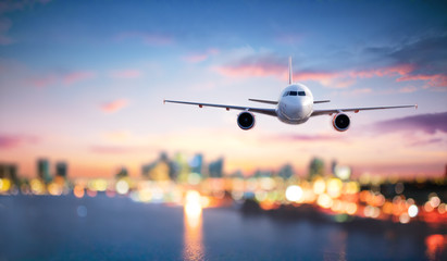 Airplane In Flight At Twilight With Blurred Cityscape
