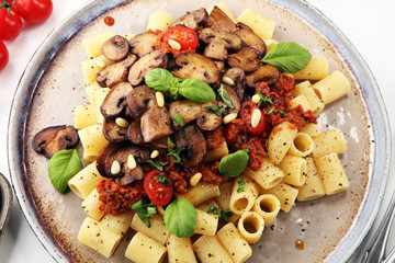 Penne pasta rigatoni in tomato sauce with mushrooms, tomatoes decorated with parsley and basil