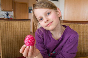 Ein 7 jahre altes Mädchen lächelt und hält ein rotes gepunktetes Osterei in die Kamera