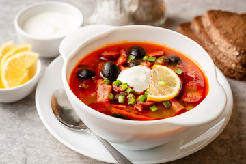 Traditional Russian meat soup Solyanka in bowl on grey stone background. Selective focus.