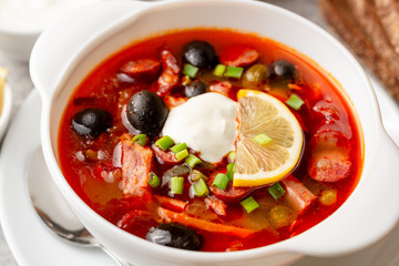 Traditional Russian meat soup Solyanka in bowl on grey stone background. Selective focus.