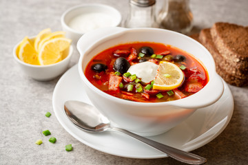 Traditional Russian meat soup Solyanka in bowl on grey stone background. Selective focus.