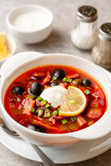 Traditional Russian meat soup Solyanka in bowl on grey stone background. Selective focus.