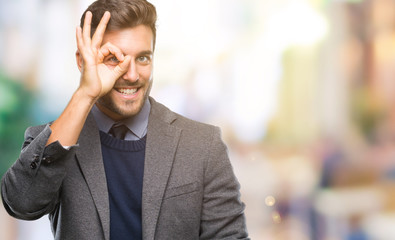 Young handsome business man over isolated background doing ok gesture with hand smiling, eye looking through fingers with happy face.