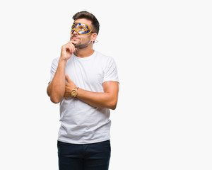 Young handsome man wearing carnival mask over isolated background with hand on chin thinking about question, pensive expression. Smiling with thoughtful face. Doubt concept.