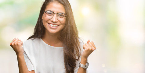 Young beautiful arab woman wearing glasses over isolated background celebrating surprised and amazed for success with arms raised and open eyes. Winner concept.