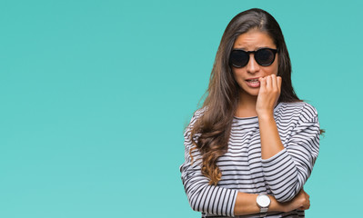 Young beautiful arab woman wearing sunglasses over isolated background looking stressed and nervous with hands on mouth biting nails. Anxiety problem.