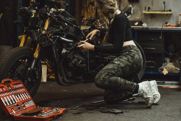 Fototapeta na wymiar beautiful girl with long hair in the garage repairing a motorcycle