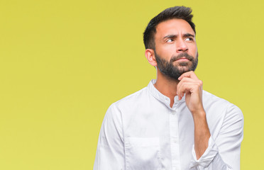 Adult hispanic man over isolated background with hand on chin thinking about question, pensive expression. Smiling with thoughtful face. Doubt concept.