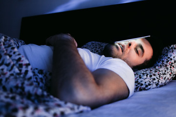Young man using smartphone in bed at night