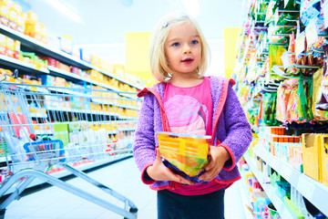 Adorable child blond girl select sweets on shelves in supermarket 