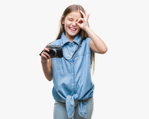 Young beautiful girl taking photos using vintage camera over isolated background with happy face smiling doing ok sign with hand on eye looking through fingers