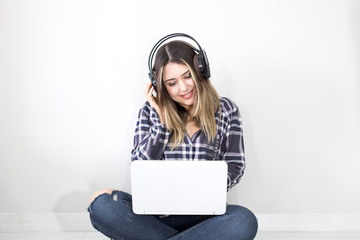 Cheerful young woman listening to music with headphones at home, working on laptop