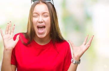 Young beautiful caucasian woman wearing sunglasses over isolated background celebrating mad and crazy for success with arms raised and closed eyes screaming excited. Winner concept