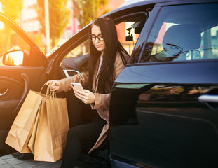 Young trendy woman with shopping bag in black vehicle on parking