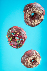 Donuts flying or falling  on blue background. Colorful and glazed donuts with sprinkles and nuts. Copy space.