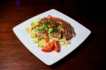 Appetizing dish on a white plate stands on a wooden table, food, snack