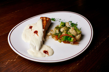 Appetizing dish on a white plate stands on a wooden table, food, snack
