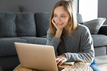 Cheerful freelance worker having video chat with customer. Young woman using laptop in her living room, staring at screen and speaking. Video call concept