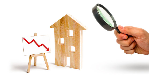 Magnifying glass is looking at the wooden house and red arrow down. concept of falling prices and demand for real estate, the fall in the rate of construction of new housing and buildings. Low quality