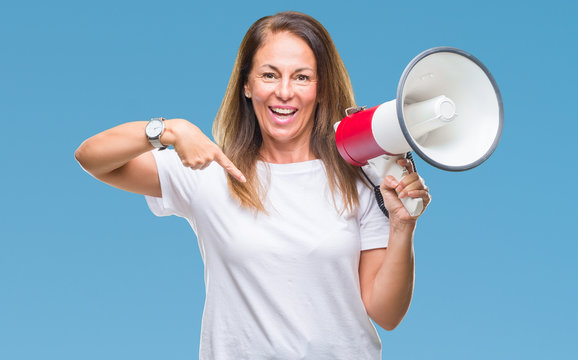 Middle age hispanic woman yelling through megaphone over isolated background with surprise face pointing finger to himself