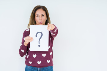 Middle age woman thinking and holding paper with question mark symbol over isolated background pointing with finger to the camera and to you, hand sign, positive and confident gesture from the front