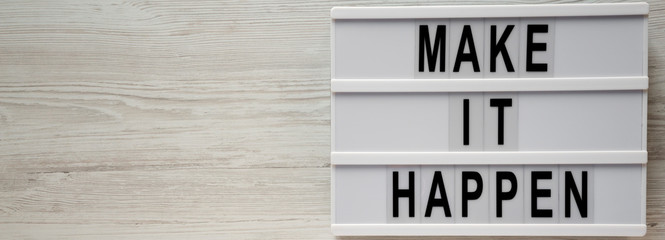 Modern board with text 'Make it happen'on a white wooden surface, top view. From above, flat lay, overhead.