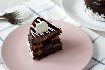 Piece of homemade chocolate cherry cake on a pink plate, side view.