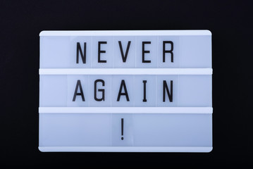 Slogan (Phrase) “Never Again” on lightbox lettering on black background.