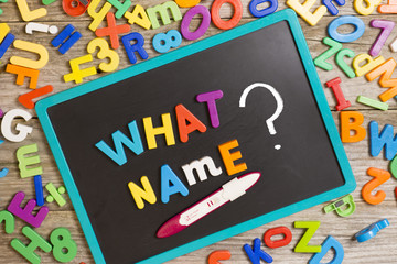 What name for a new baby, question on blackboard with many colorful plastic letters and positive pregnancy test