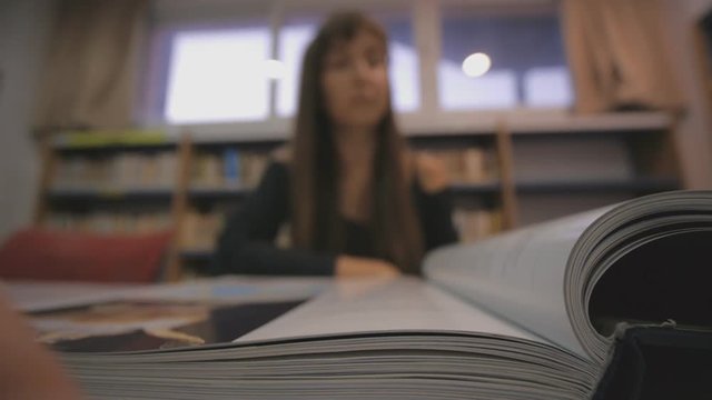 Young caucasian woman turns the page of the illustrated book in library. Focus on book spine.