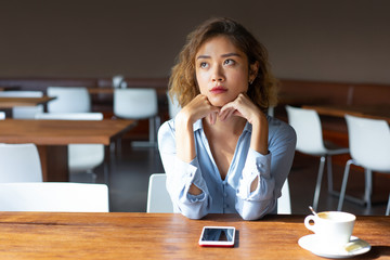 Serious businesswoman with curly hair sitting in coffee shop. Pensive Chinese lady in blouse...