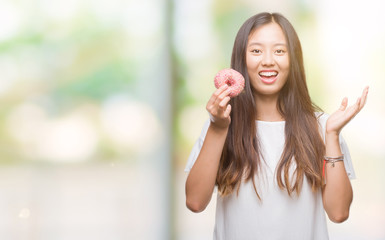 Young asian woman eating donut over isolated background very happy and excited, winner expression celebrating victory screaming with big smile and raised hands