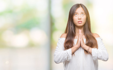 Young asian woman over isolated background begging and praying with hands together with hope expression on face very emotional and worried. Asking for forgiveness. Religion concept.