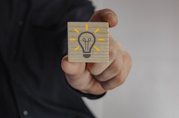 a man in a suit holds in his hand a wooden cube with a light bulb pattern that characterizes the...