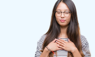 Young asian woman wearing glasses over isolated background smiling with hands on chest with closed eyes and grateful gesture on face. Health concept.