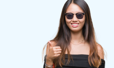 Young asian woman wearing sunglasses over isolated background doing happy thumbs up gesture with hand. Approving expression looking at the camera with showing success.