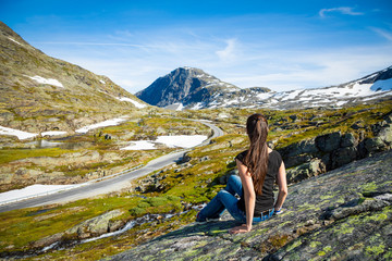Happy tourist woman looking on road to Dalsnibba viewpoint next to Geirangerfjord and mountains landscape, Norway