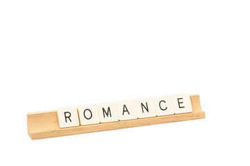 Game tiles on a wooden rack spell out the word Romance