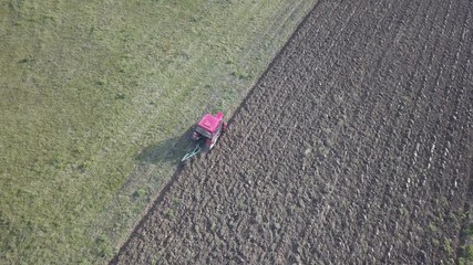 Obraz premium A farmer on a red tractor with a seeder sows grain in plowed land in a private field in the village area. Mechanization of spring field work. Farmer's everyday life. Processing of land. The agrarian.
