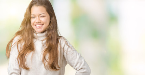 Young beautiful brunette woman wearing turtleneck sweater over isolated background winking looking...