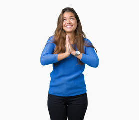Young beautiful brunette woman wearing blue sweater over isolated background begging and praying...