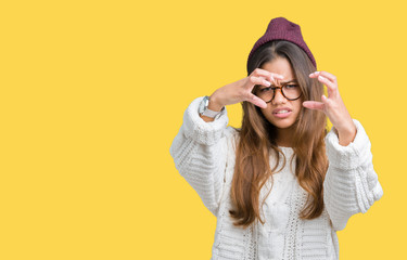 Young beautiful brunette hipster woman wearing glasses and winter hat over isolated background Shouting frustrated with rage, hands trying to strangle, yelling mad