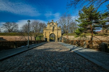 Fototapeta na wymiar Prague, Czech Republic / Europe - January 15 2019: Stone Leopolds gate at Vysehrad is a Baroque gate from Prague fortification built in 17th century, cobble stone street, sunny day, blue sky, trees