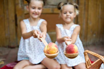 Fototapeta premium Girls hold peaches on large wooden spoons