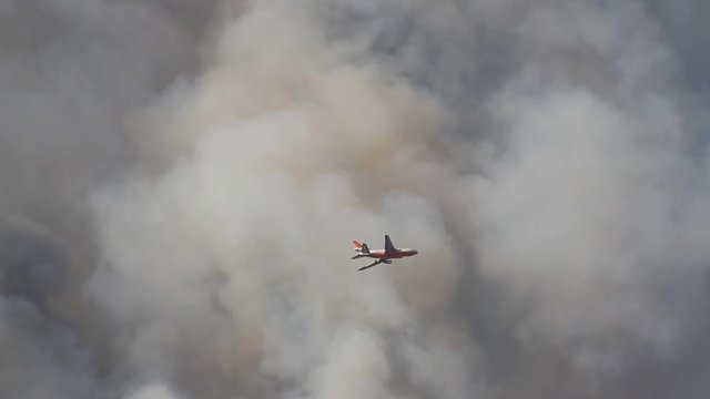 Large airplane flying through smoke fighting a California wildfire