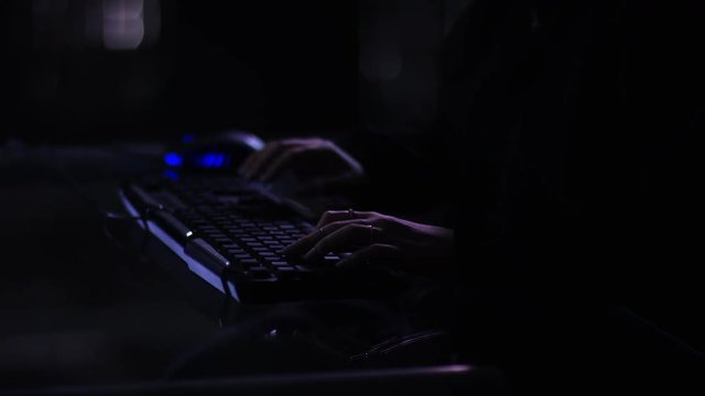 camera focuses on hooded female tyoing hacking in mysterious dark atmosphere