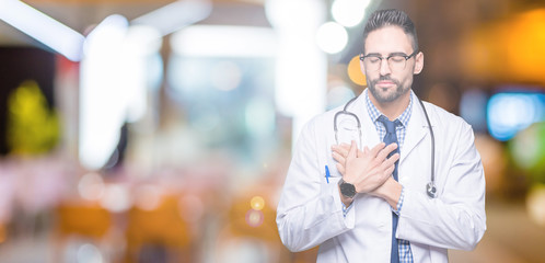 Handsome young doctor man over isolated background smiling with hands on chest with closed eyes and grateful gesture on face. Health concept.