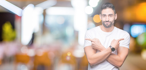 Handsome man wearing white t-shirt over night outdoors background Pointing to both sides with fingers, different direction disagree