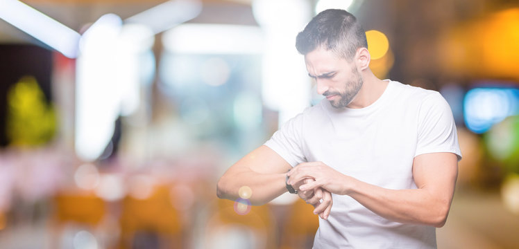 Handsome man wearing white t-shirt over night outdoors background Checking the time on wrist watch, relaxed and confident